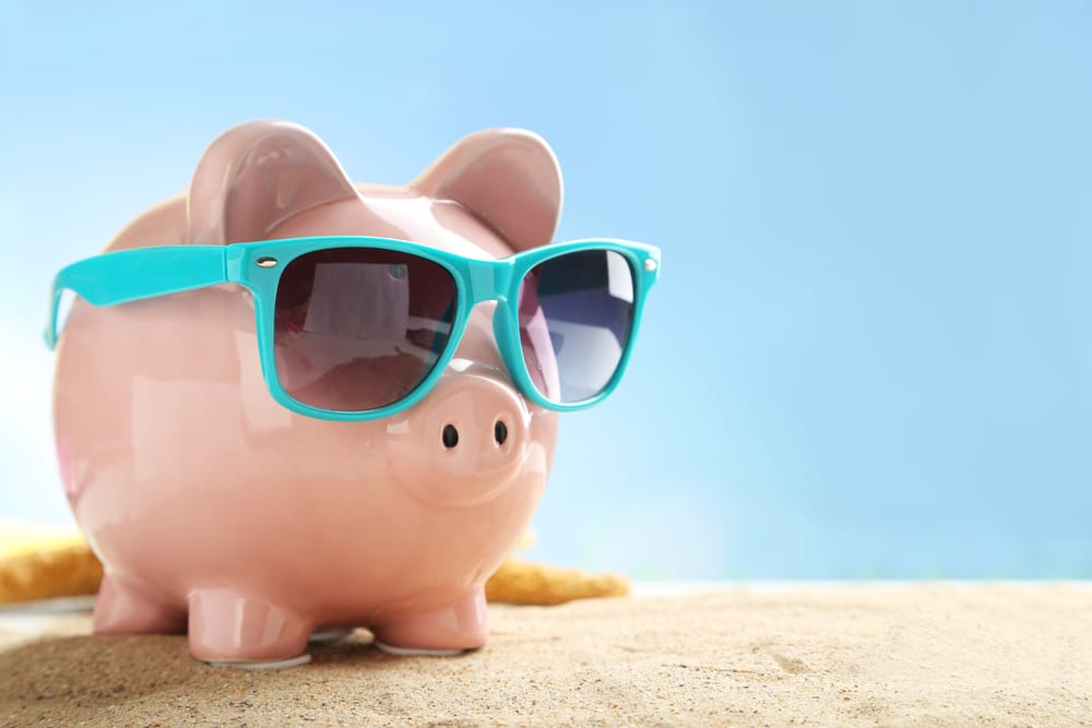 Piggy bank in sunglasses on the beach, saving for a vacation on a budget