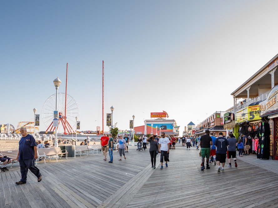 Visitors strolling the wooden Ocean City, Maryland boardwalk past shops and amusement rides