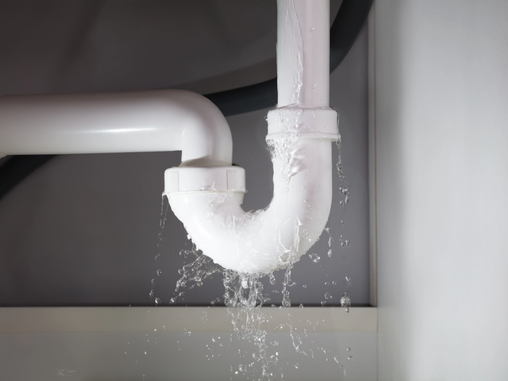 A leaking white PVC pipe under a sink, symbolizing costs covered by timeshare maintenance fees.