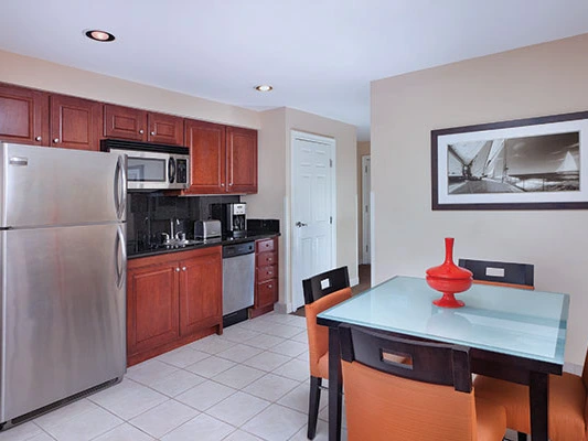 Studio kitchen featuring modern stainless steel appliances, dark wood cabinets, and a glass dining table at the Harbour Lights resort.