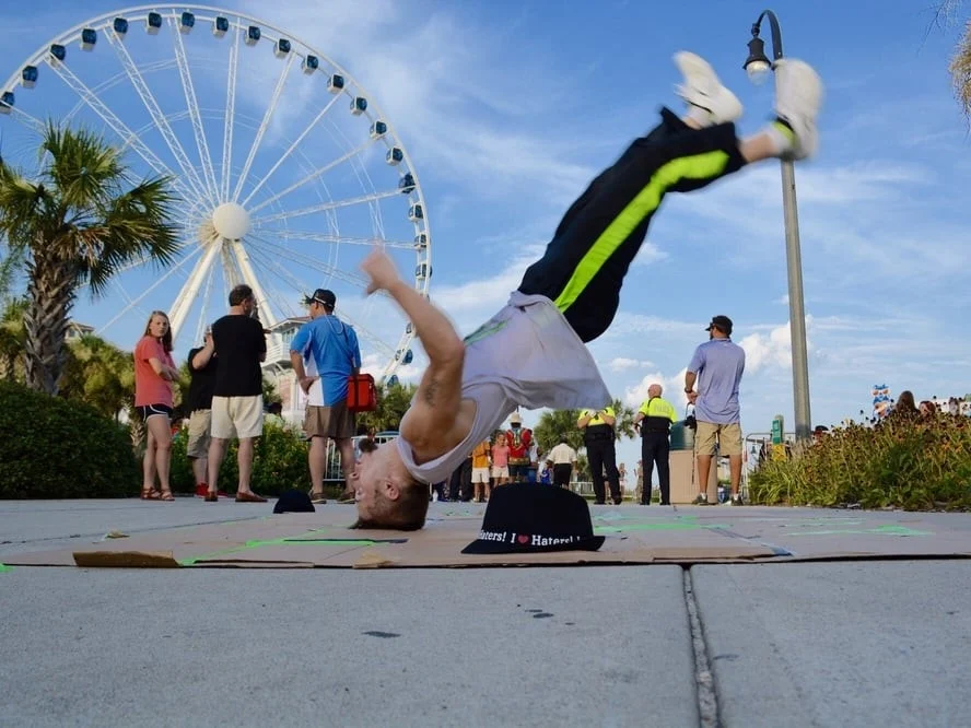 Street performer breakdancing for a crowd on the Myrtle Beach boardwalk with the SkyWheel behind