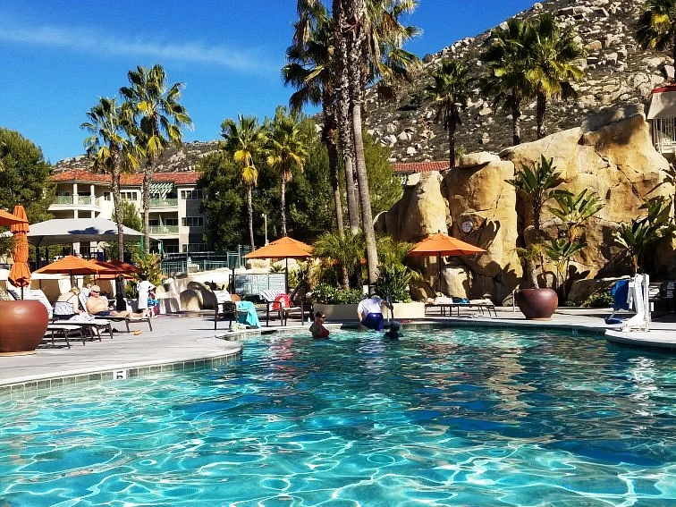 Guests enjoying the large outdoor swimming pool, natural rock features, and shaded lounge chairs at the Welk Resorts timeshare in san diego.