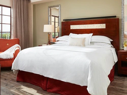 Spacious master bedroom featuring a king bed, red accents, and a comfortable reading chair at a Hilton Grand Vacations Club MarBrisa timeshare in san diego.