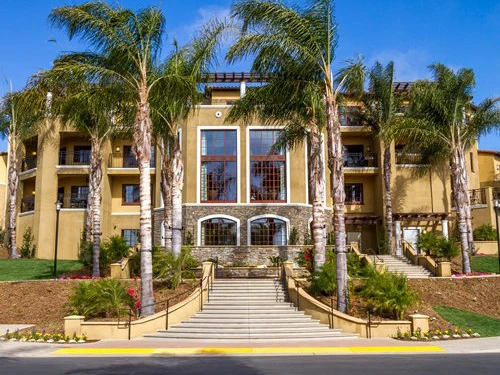 Front exterior and landscaped steps of the Hilton Grand Vacations Club MarBrisa timeshare in san diego surrounded by tall palm trees.