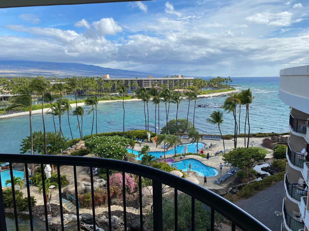 A high-angle balcony view overlooking tropical swimming pools and a palm tree-lined lagoon for warm weekend getaways.