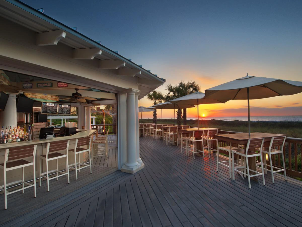 Oceanfront outdoor bar and deck seating with umbrellas at sunset, ideal for warm weekend getaways.