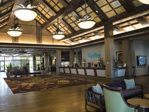 The spacious lobby of Tahiti Village Resort features high vaulted wooden ceilings, tropical chandeliers, and cozy seating.