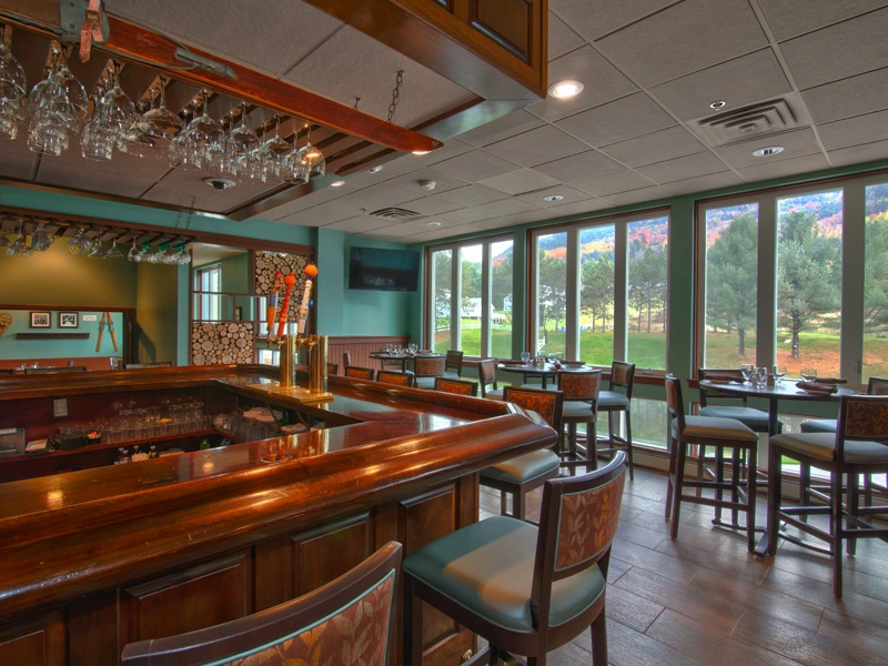 A rustic wooden bar counter and seating with large windows overlooking a green field at Mount Ascutney Resort.