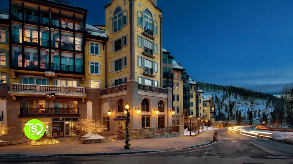 Illuminated luxury resort exterior at dusk with car light trails on an adjacent winding road.