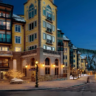 Illuminated luxury resort exterior at dusk with car light trails on an adjacent winding road.