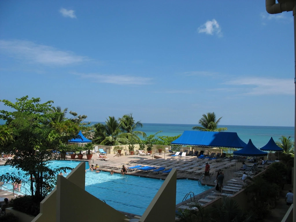 Poolside view at an RCI resort in Puerto Rico with blue canopy shades, lounge chairs, palms, and turquoise ocean beyond.