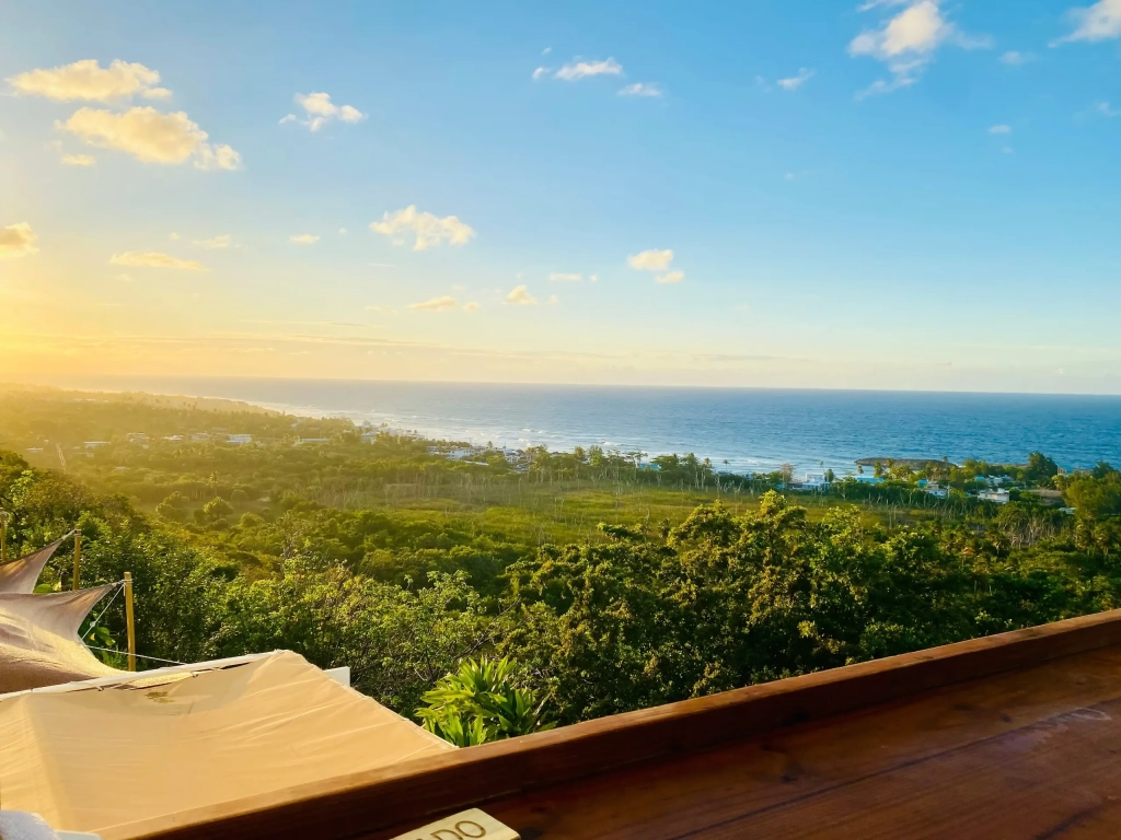 Panoramic sunset view from a wooden deck at RCI resorts in Puerto Rico, overlooking lush tropical treetops and calm ocean coastline.