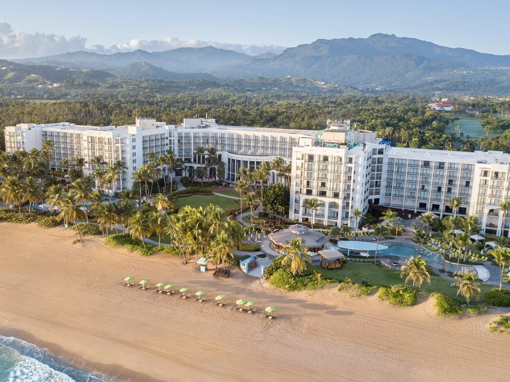 Aerial view of an RCI resort in Puerto Rico featuring white beachfront buildings, palm trees, and a pool area.