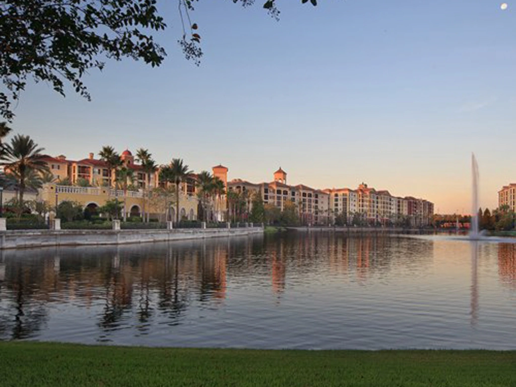 Tuscany Village resort buildings reflecting across a calm lake with a fountain.