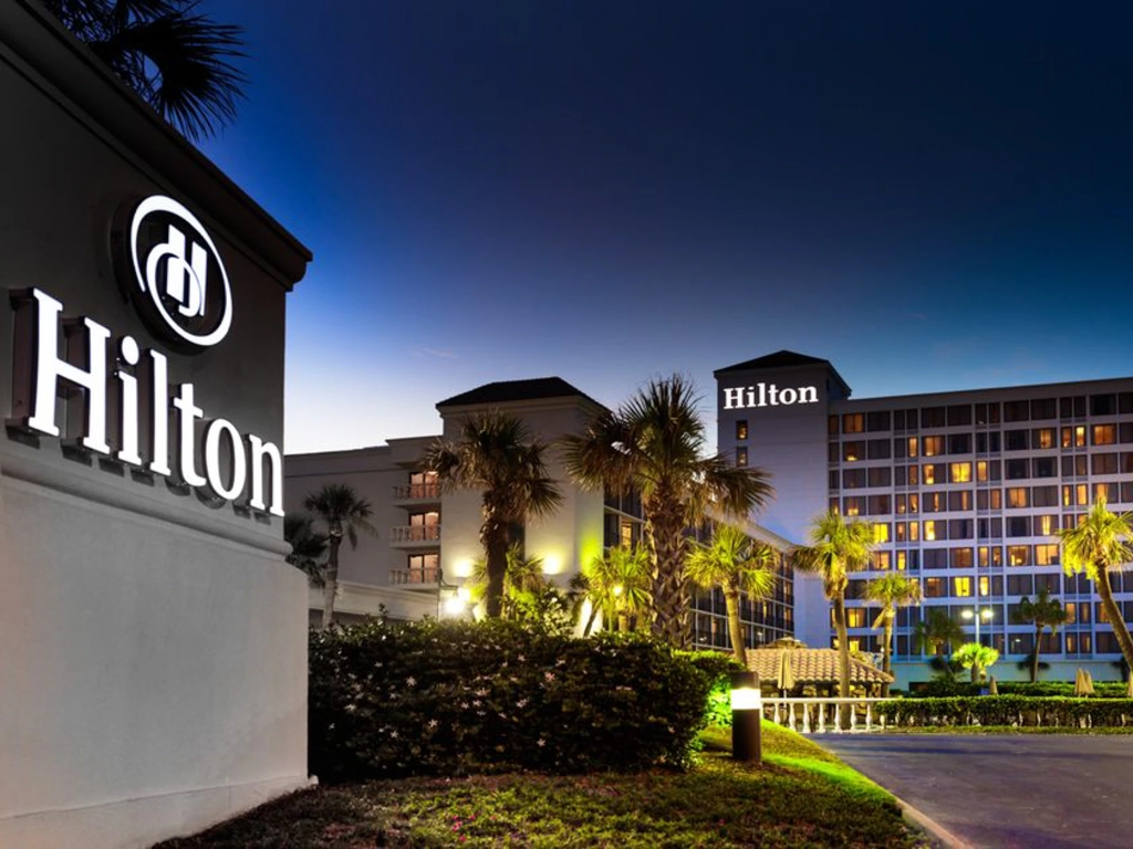 Illuminated exterior facade and palm trees at Galveston Island Resort during dusk.