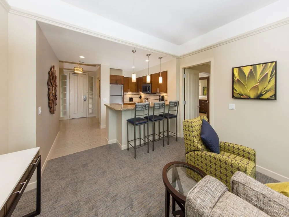 Open-plan suite at Marriott's Desert Springs Villas II with a green patterned armchair, kitchen bar, and pendant lights.