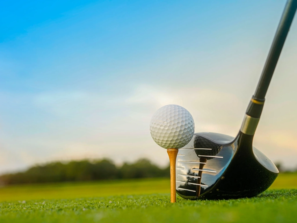 Golf ball on a wooden tee with a driver club head positioned behind it on a green fairway.