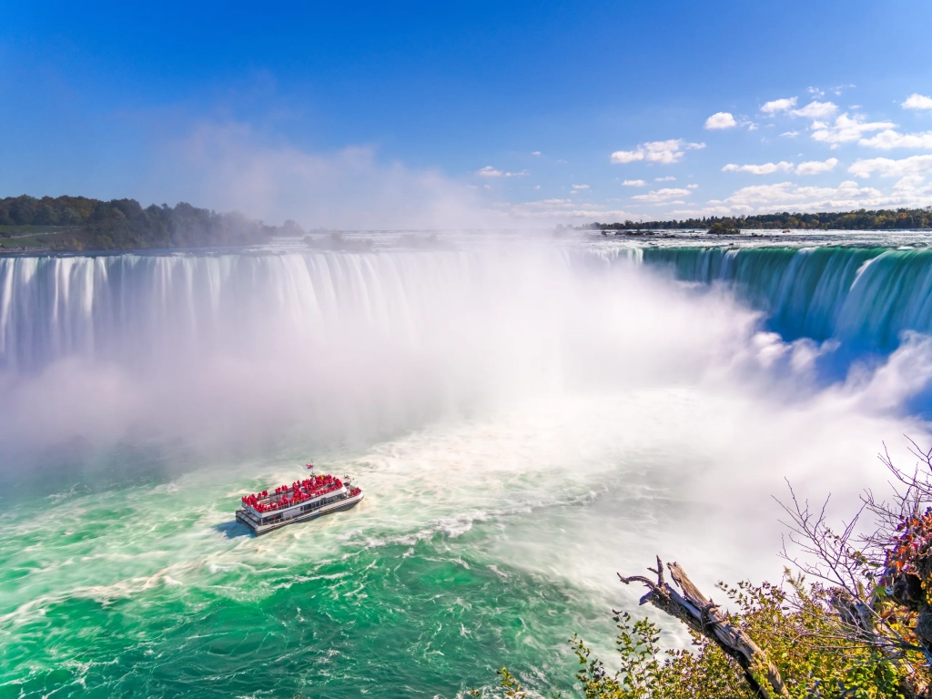 Tour boat filled with passengers in red ponchos approaches the base of Horseshoe Falls at Niagara Falls.