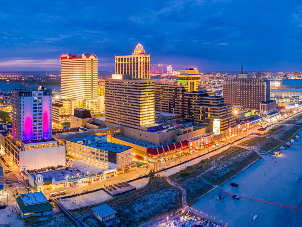 Aerial dusk view of one of the best boardwalks on east coast, with Atlantic City casino hotels glowing above the sandy beach.