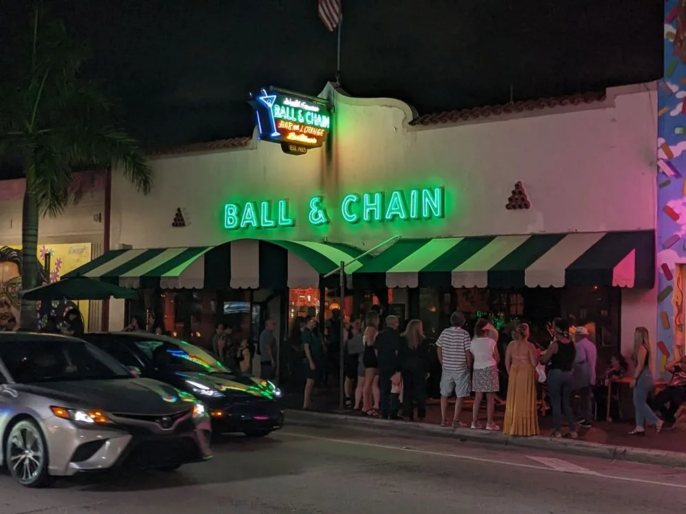 Crowd enjoying Things To Do in Miami At Night outside Ball and Chain bar beneath a glowing green neon sign.