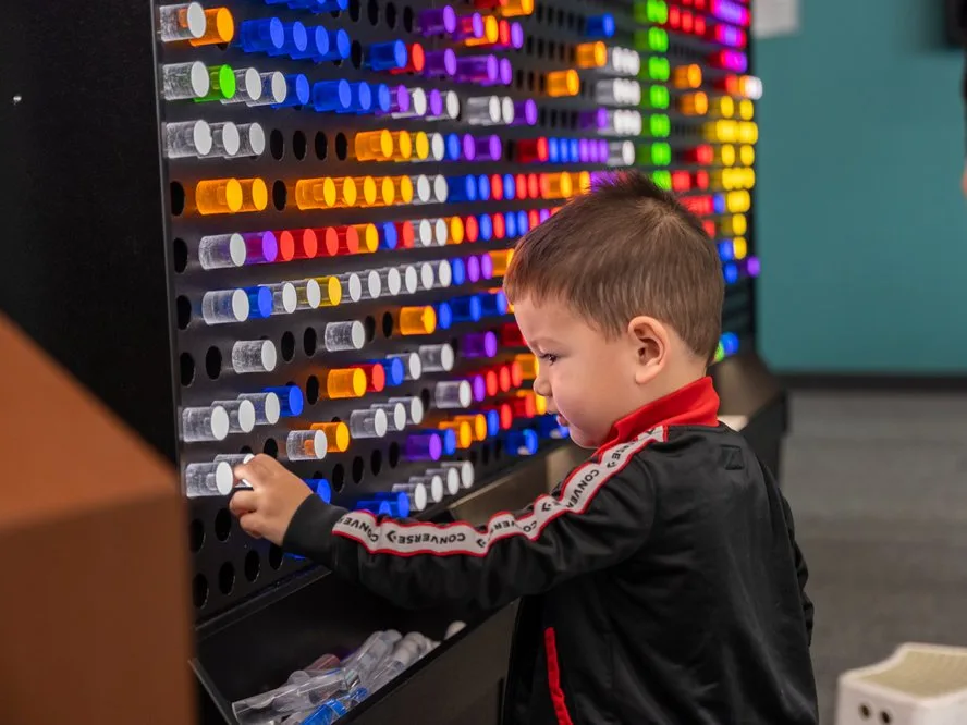 Young boy enjoying kid friendly Los Angeles museum fun with colorful pegs on a large backlit activity wall.