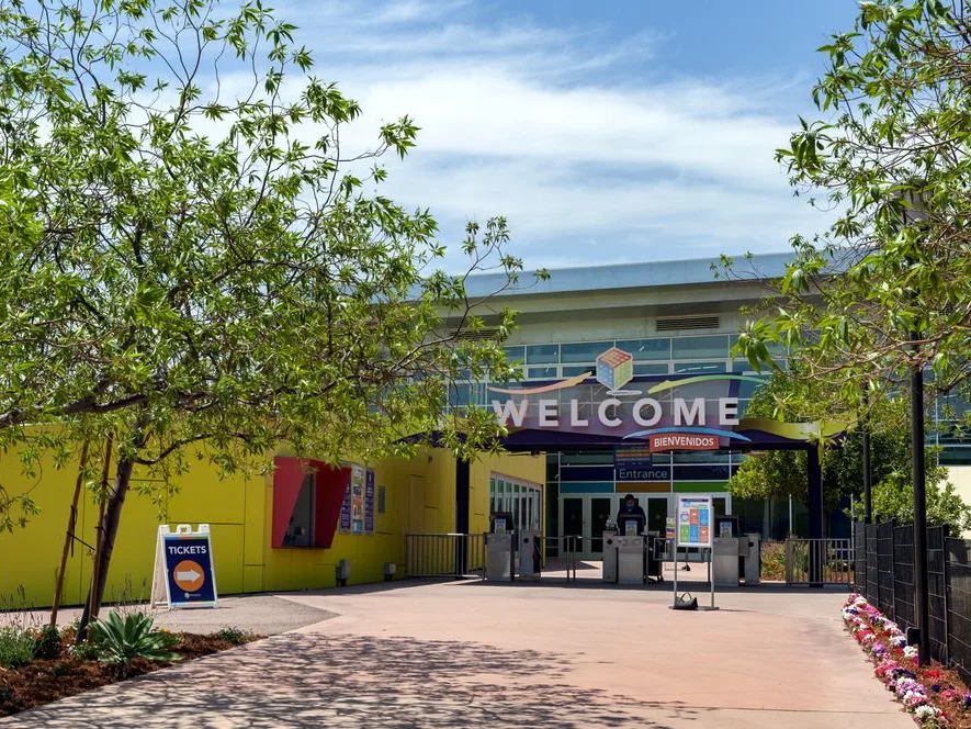 Entrance to Discovery Cube, a kid friendly Los Angeles science museum, with a Welcome sign, ticket booth, and colorful yellow walls.