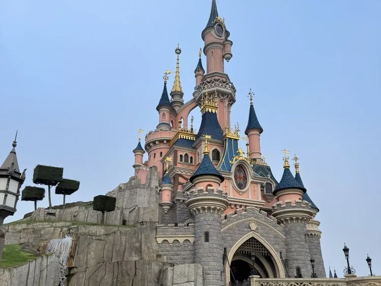 Sleeping Beauty Castle at Disneyland Paris, one of the best theme parks in the world, with pink towers, gold accents, and a pale blue sky.