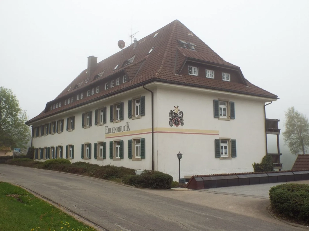 Erlenbruck building with white facade, dark shutters, and steep tiled roof on a foggy day in Germany.