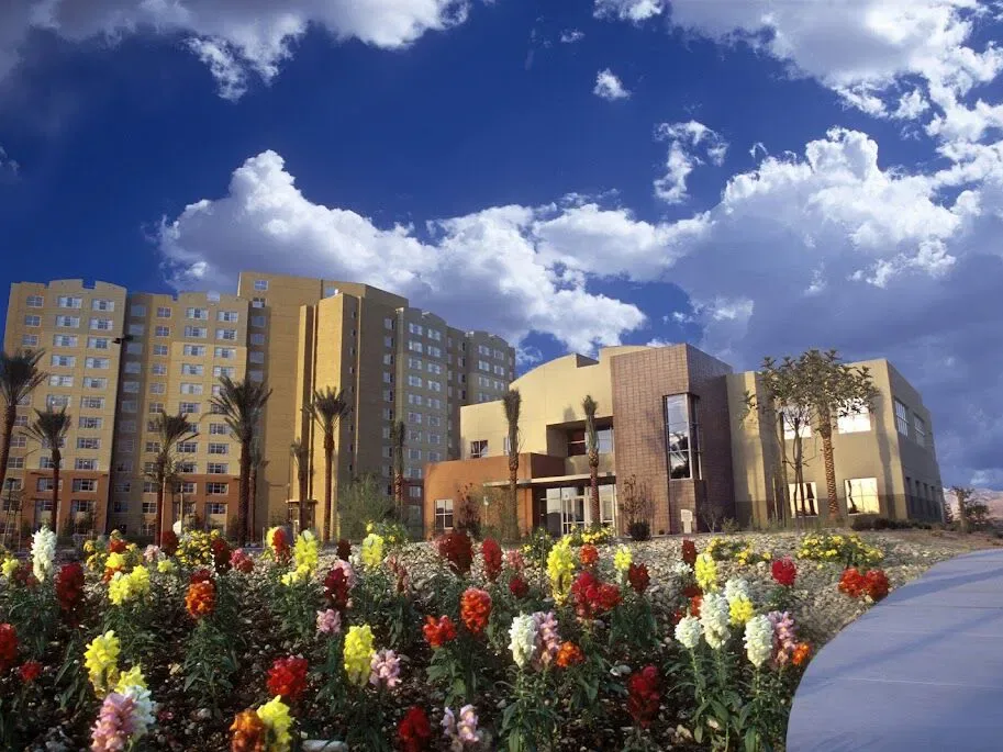 Colorful flower garden outside a multi-story vegas timeshare resorts complex with palm trees under a bright blue sky.