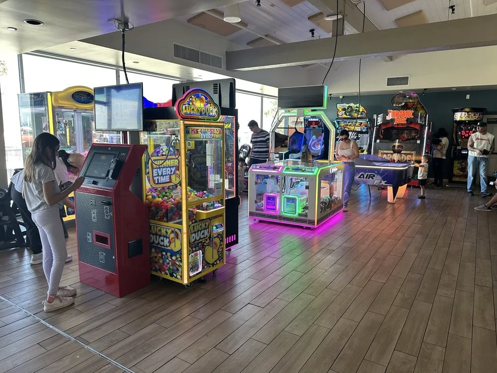 Kid friendly Los Angeles arcade with colorful claw machines, ticket kiosks, and air hockey tables on a wood floor.
