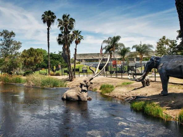 Life-size mammoth sculptures rising from dark tar pits at La Brea Tar Pits, a kid friendly Los Angeles attraction surrounded by palm trees.