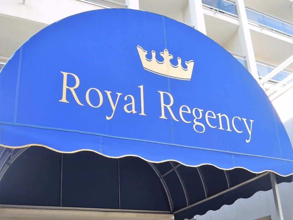 Blue domed awning with gold crown logo and Royal Regency name at a hotel entrance.