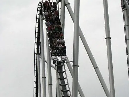 Riders plunge down a steep drop on a steel roller coaster under an overcast sky at one of the best theme parks in the world.