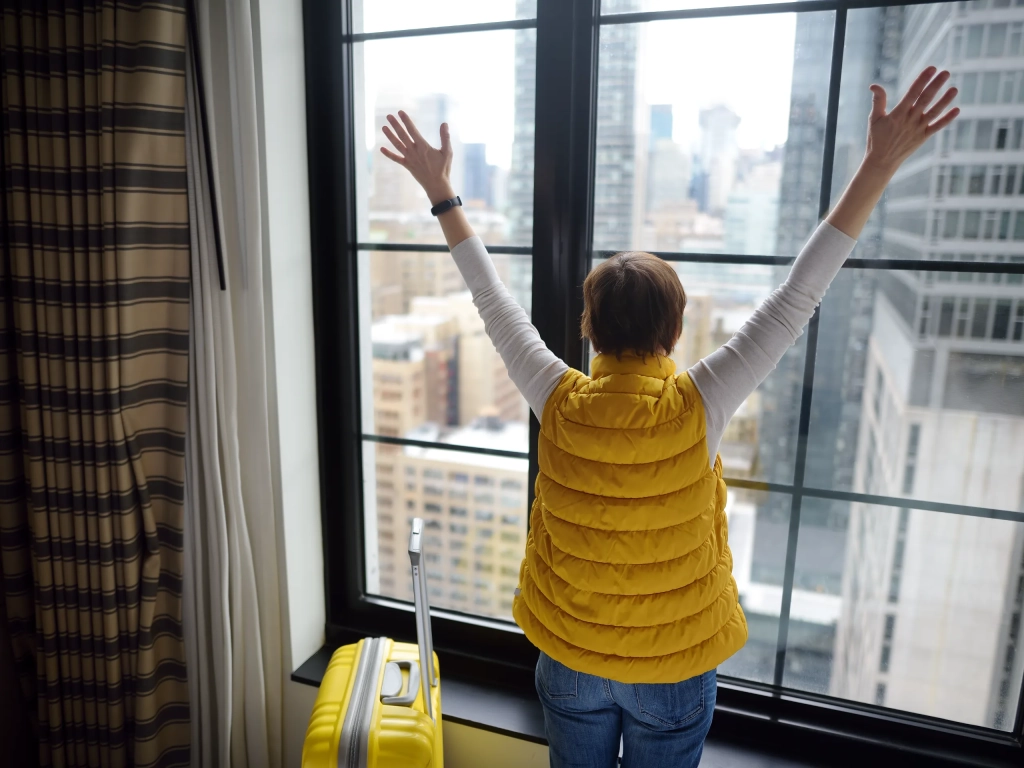 Traveler with a yellow suitcase taking in the city from a high-rise window