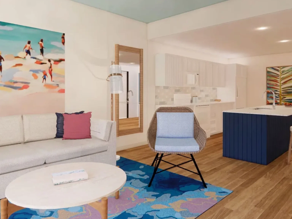 Open-plan living room and kitchen with a white sofa, wicker chair, blue area rug, and navy kitchen island.