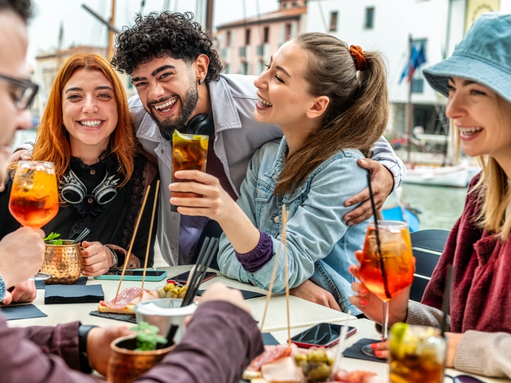Friends laughing over cocktails and snacks at a harborside table