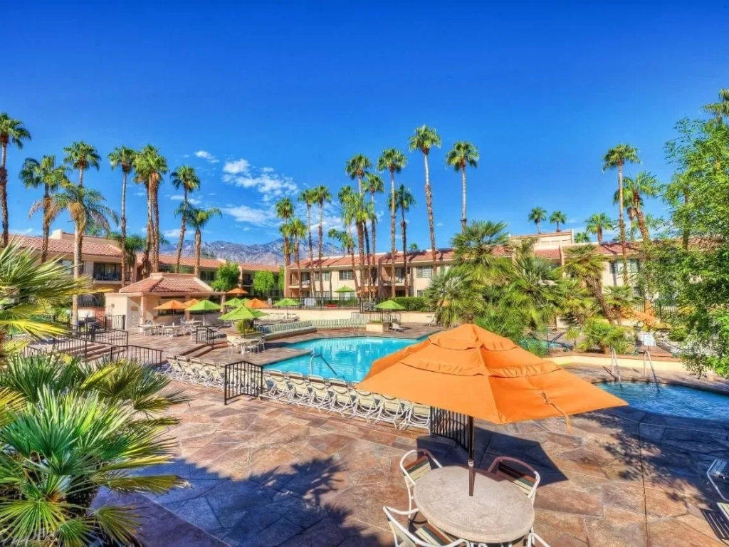 Resort pool with lounge chairs and palms at Hyatt Vacation Club at Desert Oasis, set against mountain views.