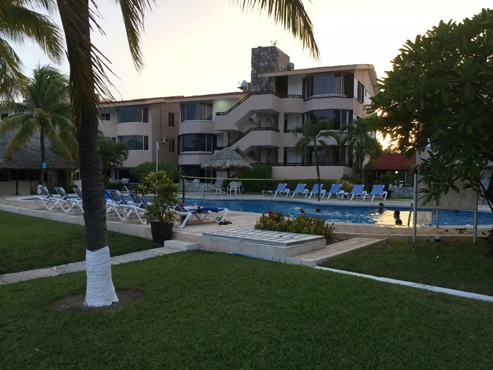 Outdoor vacation rentals pool area with lounge chairs, palm trees, and a multi-story building glowing at sunset.