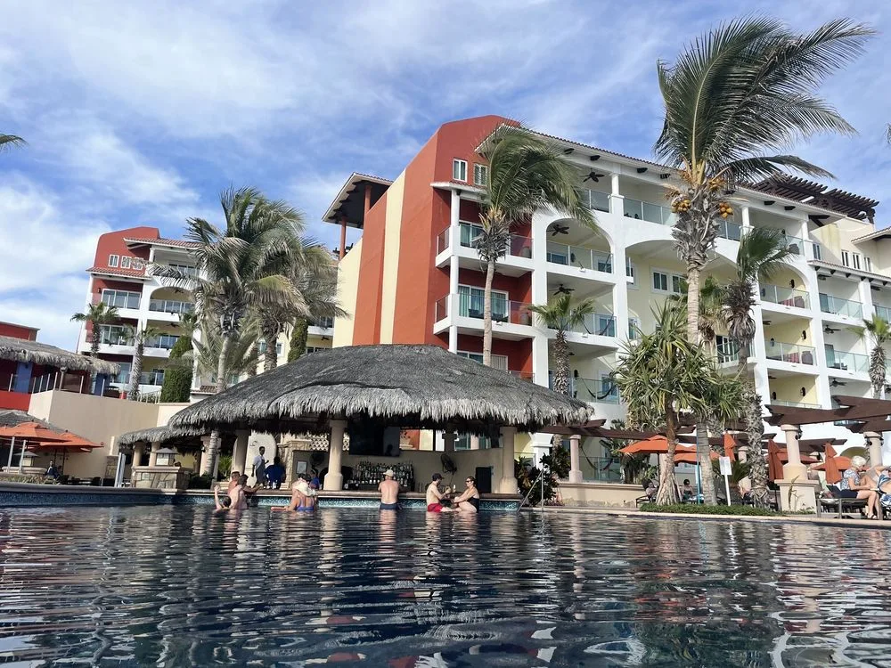 Guests enjoy the pool at Hyatt Vacation Club at Sirena del Mar, with a thatched swim-up bar, palm trees, and colorful resort buildings.