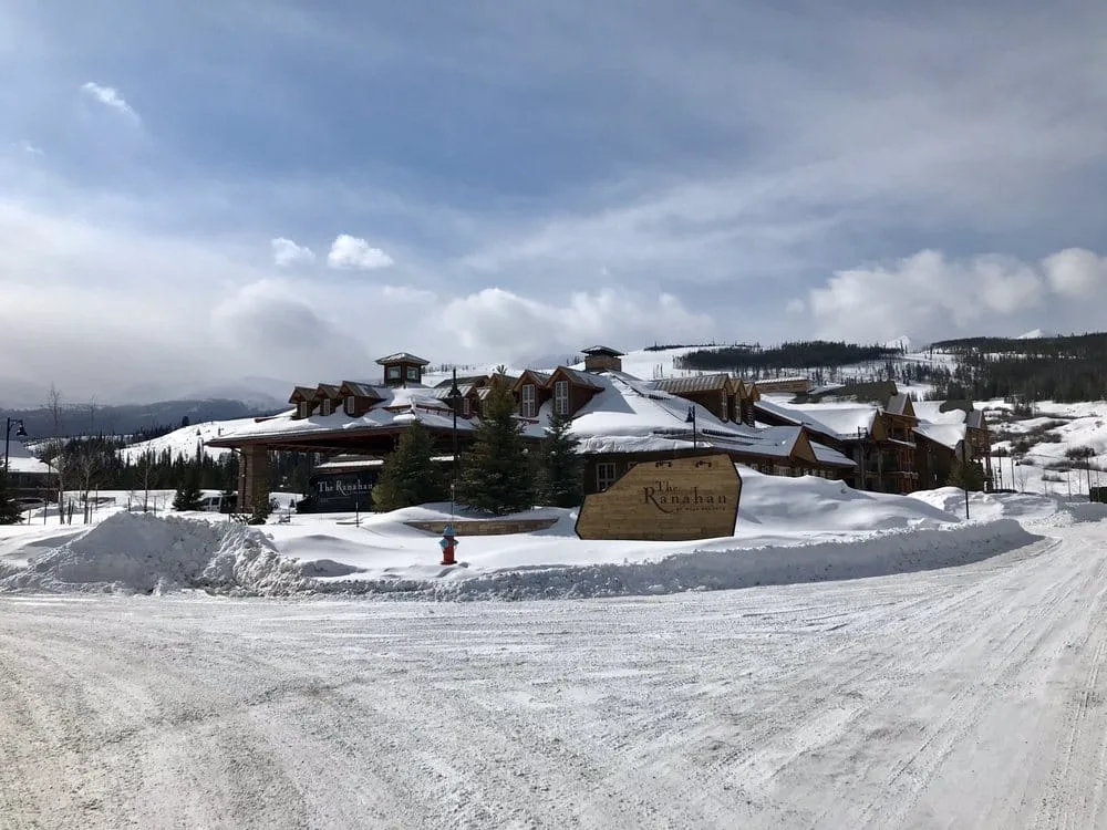The Ranahan mountain lodge surrounded by deep snow with ski slopes visible in the background on a cloudy winter day.